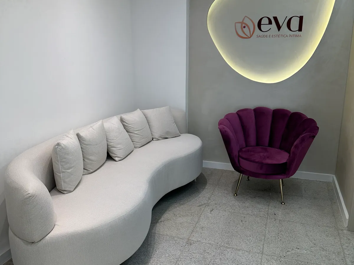 Sala de espera da clínica Eva com sofá curvo, poltrona de veludo e logotipo iluminado na parede
